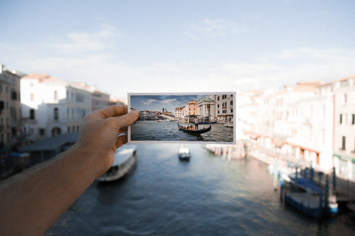 Person holding postcard with Venice canals on in front of Venice Canals, Italy