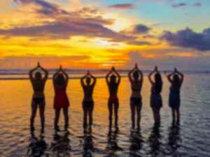 A row of people on a beach doing a yoga pose at sunset