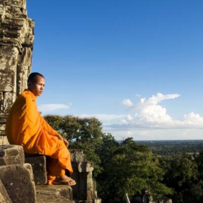 Monk in orange robe sitting on ledge at Angkor Wat