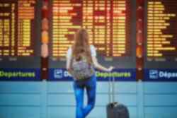 A person with a suitcase looking up at an airport departures board