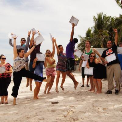 Group at graduation ceremony jumping in the air holding certificates on the beach