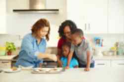 Two people baking with two kids watching on