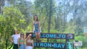 Group of travellers with a bike at 'Welcome to Byron Bay' Sign, Byron Bay, Australia