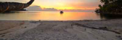 A lone boat sits in the water on a deserted beach at sunset