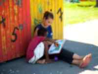 A volunteer and a child sitting in the shade reading a book