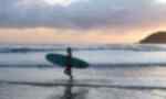 A traveller walks along a beach at sunset while waves crash at her feet