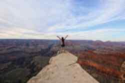 Person stands at a peak with arms outstretched overlooking the Grand Canyon