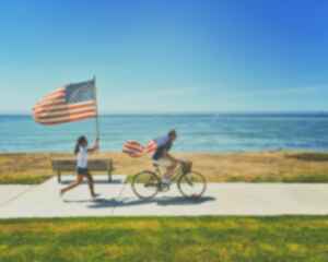A person cycling with an American flag as a cape, followed by a person holding an American flag