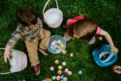 Two children sitting on grass with easter baskets and plastic eggs