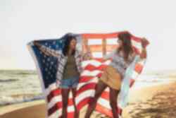 Two people on the beach holding a large American flag