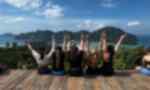A group of travellers sit on a platform overlooking the ocean and islands while doing peace hand signs 