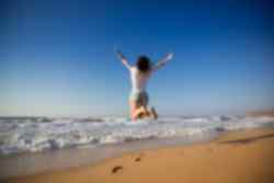 A traveller mid-jump on a beach with crashing waves