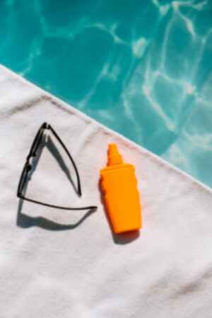 Suncream and sunglasses next to swimming pool