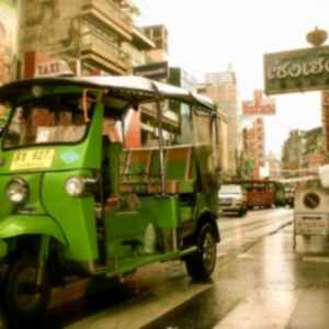 A green Tuk Tuk driving down a busy street in Chinatown in Bangkok