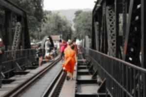Children in bright orang monk robes walk along train tracks over a bridge