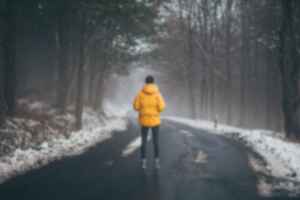 Person in yellow jacket standing on an icy road between snow-capped trees